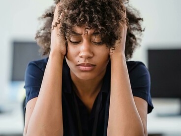Portrait of a tired woman sitting at a desk, touching her face while lost in deep thought