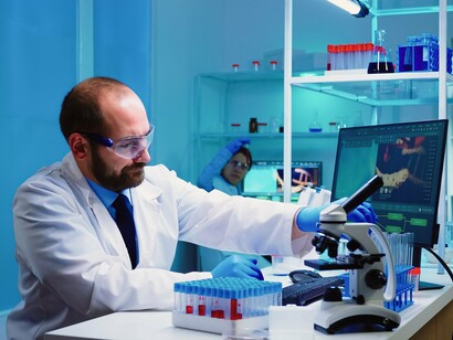 A scientist examining biological samples beside digital data displays, representing the transformation of biomedical research through AI