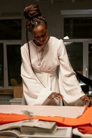 A fashion designer stands at her workspace, arranging and examining fabrics