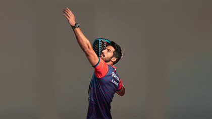 Athletic padel player getting into position for a shot on an indoor glass court