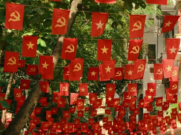 Bandeiras com símbolos comunistas penduradas de forma decorativa em uma rua, compondo um cenário marcado pela expressão política em espaço público. No artigo, a imagem dialoga com as reflexões do autor sobre ideologias, polarização e os desafios éticos e morais que, em sua visão, marcam a sociedade contemporânea