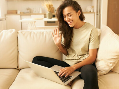 A young female user waves at her computer screen, illustrating the emerging role of AI therapy in mental health support