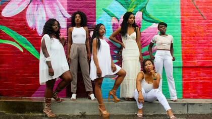Six African American women dressed in white pants pose together in the USA