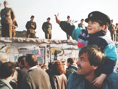 Niño en los hombros de su padre saluda a los militares que custodian el Muro de Berlín el día de su caída el 9 de noviembre de 1989, Berlín, Alemania