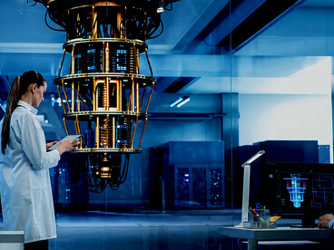 In a futuristic scientific laboratory, a professional computer engineer in a white coat studies a quantum computer while reviewing research and development analytics on her tablet