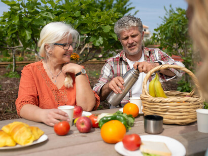 In Portugal, a happy senior couple shares a cheerful picnic surrounded by fresh fruits and vegetables in a lush garden