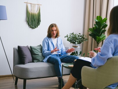 A man in a blue shirt sitting on a sofa speaking to a therapist 
