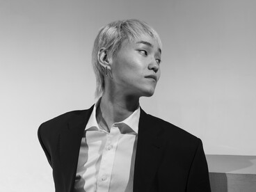 Black-and-white medium shot portrait of a young man against a clean, empty background, emphasizing mood, isolation, and minimalist composition