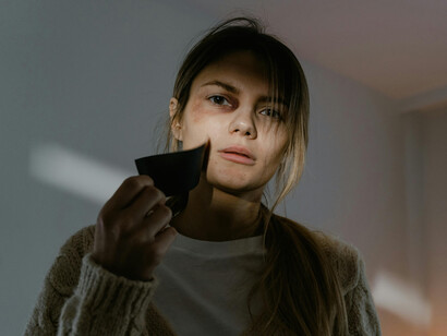 Portrait of a woman with bruises removing tape from her mouth, representing the struggle to speak out against oppression