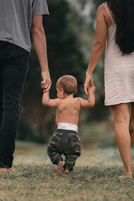 A couple walks barefoot through the garden, holding hands with their child