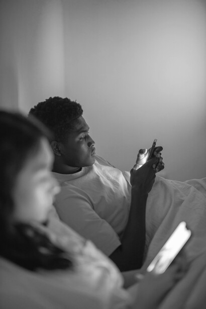 A couple lying in bed, each focused on their phones, highlighting disconnection and loneliness in the digital age