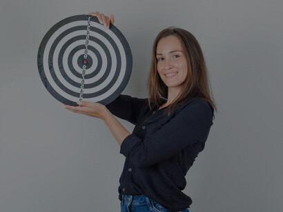 A young woman in casual attire, aiming optimistically at a dartboard with her finger