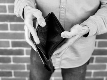 An empty black wallet held open against a brick wall starkly illustrates the economic hardship brought on by political decisions