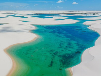 Dunas de areia branca se estendem até o horizonte, recortadas por lagoas de águas azul-turquesa sob um céu amplo. A paisagem traduz a tranquilidade e a sensação de liberdade que acompanham a caminhada narrada pelo autor