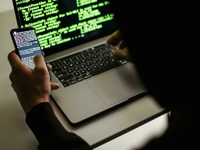 An unrecognizable developer focused on a laptop and phone with a powerful custom PC nearby