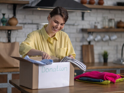 A woman seated on the floor, sorting and packing clothes for donation during a mindful wardrobe decluttering session