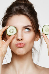 A woman in a tranquil spa setting, gently placing cucumber slices over her eyes, surrounded by luxurious skincare products like creams and oils