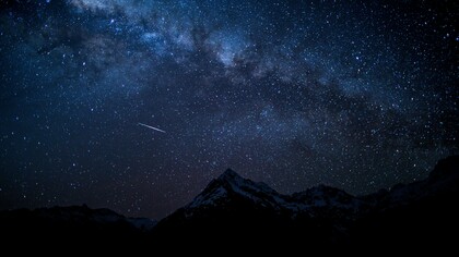 A meteor streaking across the Milky Way above mountains, representing the excitement of peak meteor shower season