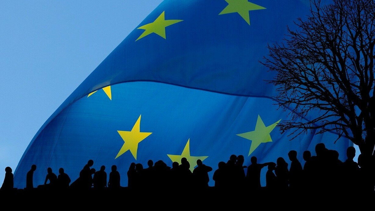 Bandiera europea con sagome di persone sullo sfondo. L'arte dell'ironia europea: scopri come una cartolina degli anni '80 ha descritto con umorismo i caratteri nazionali dei paesi della CEE, dalla cucina britannica alla sobrietà irlandese