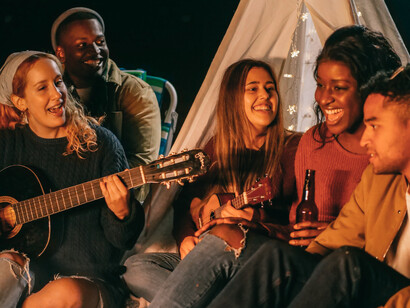 Five friends have a sing-along on the beach, having fun and laughing together