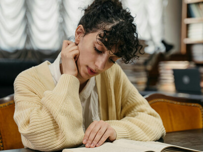 A woman wearing a knitted cardigan is reading a book in the library
