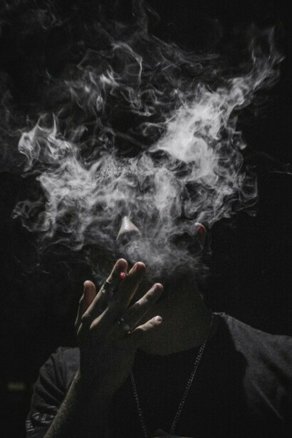 Someone in a black long-sleeve shirt stands smoking quietly