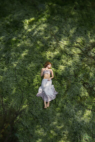 A girl lies on the grass in a garden, viewed from above, lost in quiet reflection