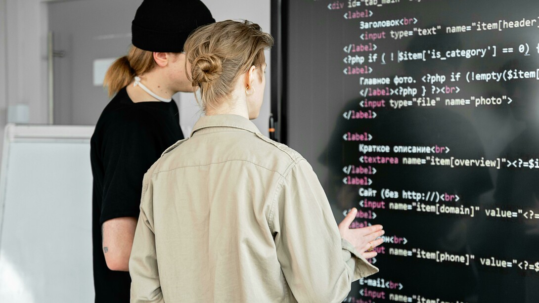 Two men reviewing code on a board, illustrating collaborative coding and the use of AI tools in development