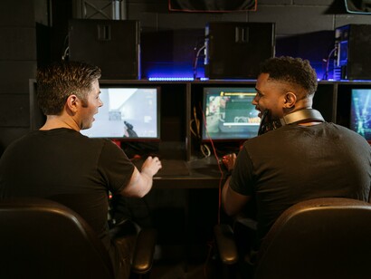 Two friends sat at computers talking to each other 