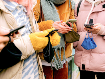 Varias personas consultan sus teléfonos móviles mientras esperan o se desplazan