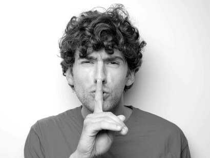 A man is angrily gesturing for silence by placing his finger over his lips