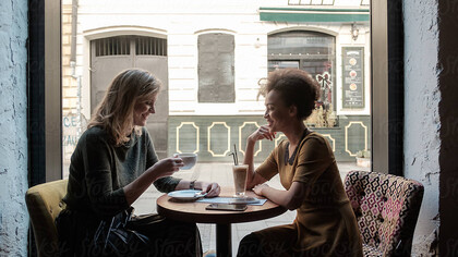 Two women share an emotional reunion in a café, laughing together