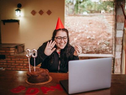 A woman marking her 30th birthday with a smile, connecting online through her laptop, embracing the freedom and independence that define this new chapter