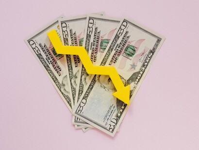 A yellow downward-pointing arrow overlays a fan of fifty-dollar bills, visually representing the economic decline and potential recession under Trump's policies