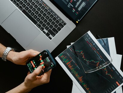 A person holding a phone looking at data next to a print out and a computer