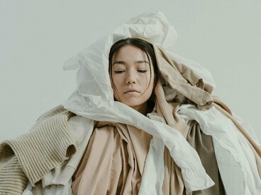 Mulher cercada de peças de roupa. A moda sustentável surge como uma alternativa consciente para reduzir os impactos de uma das indústrias mais poluentes do mundo. Isso vai além de escolher fornecedores éticos e oferecer um preço justo à mão de obra – envolve também reaproveitar tecidos e materiais descartados, reduzir o desperdício e buscar soluções com menor impacto ambiental e social