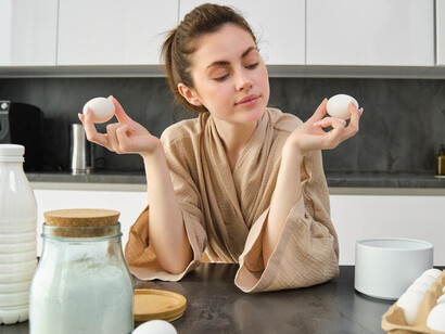 In the kitchen, a girl is making dough for cakes and cookies, following a recipe book, with milk and butter ready for baking