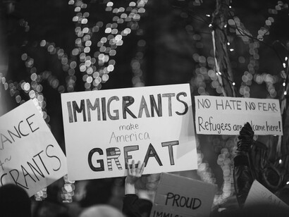 Protesters hold signs championing immigrant dignity and inclusion, a stark rebuke to the weaponization of immigration policy used to distract from elite corruption and erode constitutional order