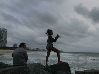 Una joven toma una foto del mar agitado desde la costa de Miami Beach