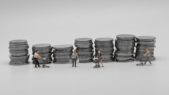 Miniature di consumatori con carrelli della spesa davanti a pile di monete: una rappresentazione simbolica del rapporto tra consumo, denaro e potere d'acquisto