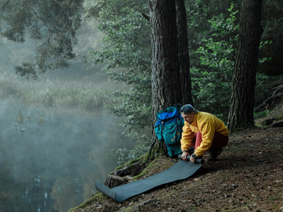 A man in yellow rolling camping equipment besides a lake