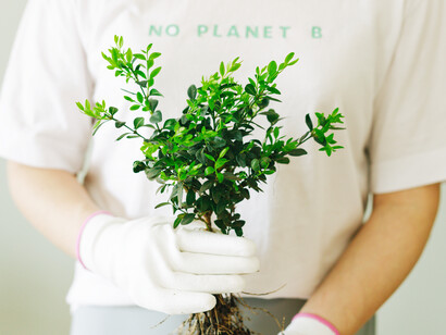 A woman holds a plant, wearing a no planet B t-shirt