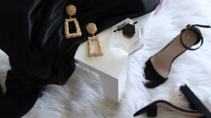 A pair of gold-colored earrings resting on a table, accompanied by black ankle-strap pumps placed on an area rug