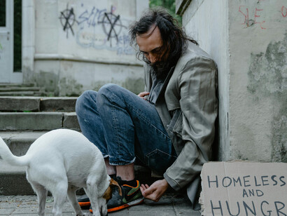 A homeless man in the USA sits beside a white short coat, wearing blue denim jean