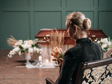 A woman mourns the loss of a loved one at a funeral, surrounded by flowers and remembrance