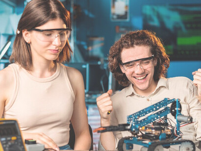Young man and woman in protective glasses conducting robotics experiments in a laboratory, highlighting human creativity and the synergy between humans and robots