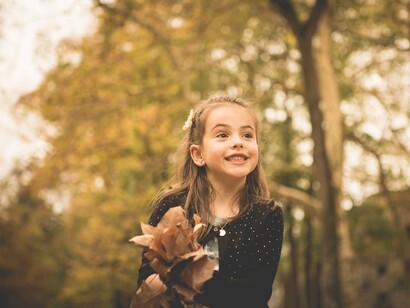 Una niña juega con las hojas caídas en otoño