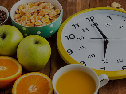 A representation of intermittent fasting: a nutritious homemade breakfast with muesli, apples, fresh fruits, and walnuts, set beside a clock on the table