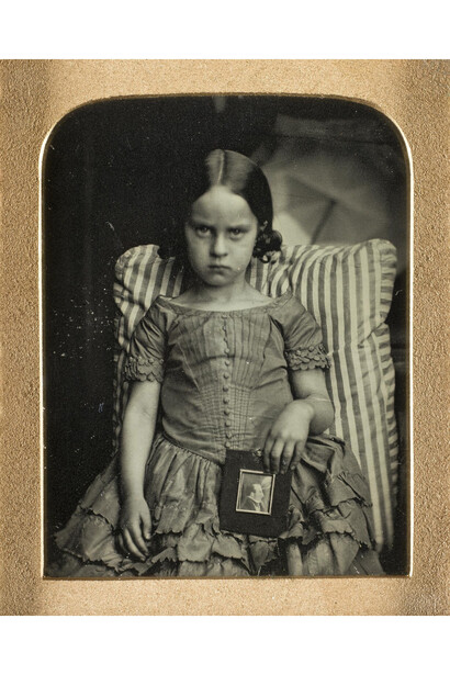 Part of The Howarth-Loomes Collection. 19 plate daguerreotype of a little girl on a striped cushion holding a framed daguerreotype of a man, possi
