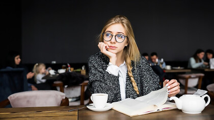 A cheerful woman sits in a cozy café, engrossed in a book, radiating warmth and joy as she enjoys her peaceful moment surrounded by the inviting ambiance